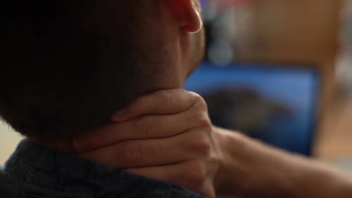 Closeup Back View of Exhausted Young Man Experiences Severe Pain in Neck Rubbing It to Relieve