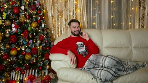 Man Relaxing by Christmas Tree Talking on Phone