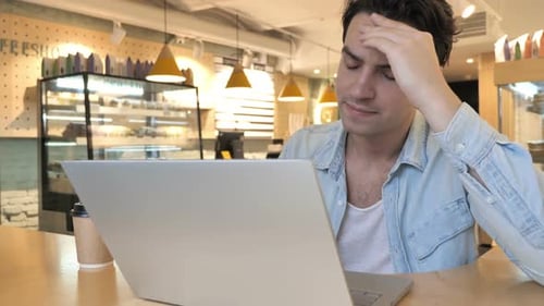 Stressed Man Working on Laptop in Coffee Shop