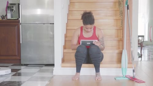 Young Woman Uses Tablet While Robot Vacuums House