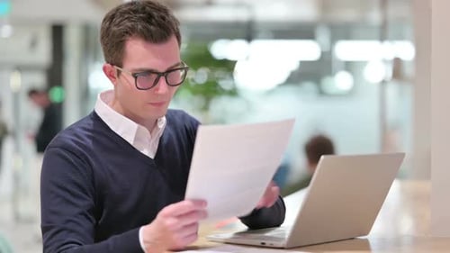 Young Adult Reviews Documents While Using Laptop