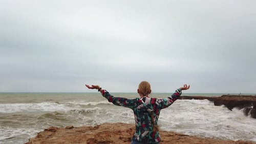 Woman Embracing Coastal Winds on Rocky Shoreline