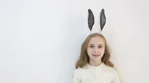 Lächelndes kleines Mädchen in einem Umhang in den Ohren eines Osterhasen, auf das ein glückliches Kind wartet