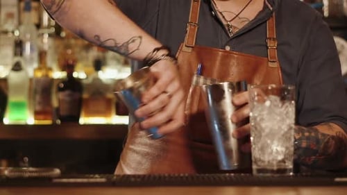 Un hombre de pie detrás de un estante de bar está transfundiendo un cóctel de una taza a otra
