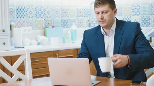 Man Works on Laptop in Kitchen, Takes Call