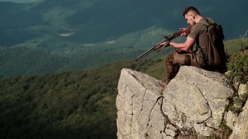 Hunter Sits Atop Rocky Mountain with Rifle
