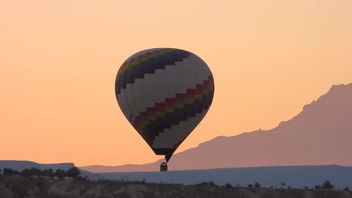 Hot Air Balloon Flying Over Rugged Landscape at Sunrise