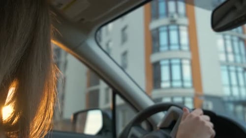 Rear View of Female Driver Behind Steering Wheel Driving a Car on a City Street