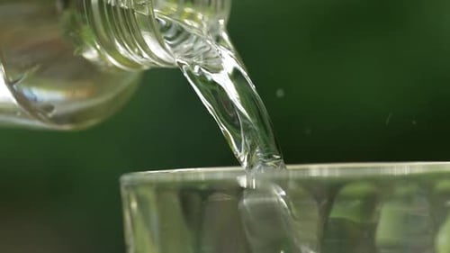 Pouring Clear Liquid from Glass Bottle into Glass