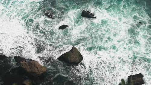 Luftbild: 4K-Wellen brechen auf dunklen Felsen in Strandnähe. Meereswellen auf den Steinen