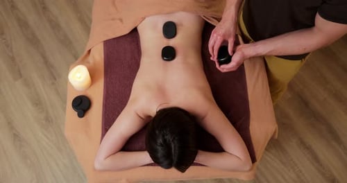 Top View of Young and Beautiful Woman Gets Hot Stone Massage Therapy in the Spa Salon