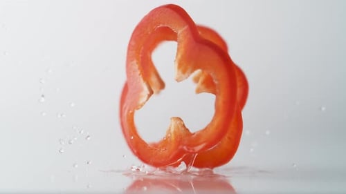 In Scheiben geschnittener roter Pfeffer fällt auf die Wasseroberfläche. Zeitlupe.