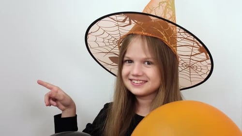 Little Girl in Orange Witch Hat Pointing Finger on Place for Text