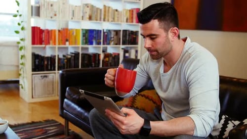 Man on Tablet Drinks Coffee at Home