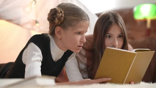Excited Absorbed Teenage Girls Reading Book Talking Lying Indoors at Tent in Living Room
