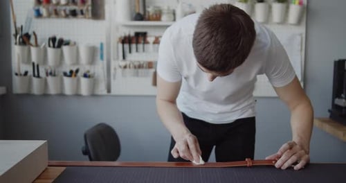 Man Conditioning Leather Belt in Bright Workshop