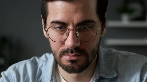 A man sits in front of a monitor close-up, Charts and tables are reflected in glasses and eyes