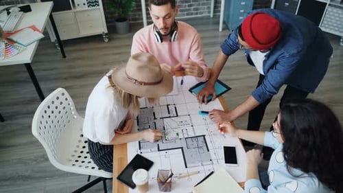 Hochwinkelansicht junger Architekten, die sprechen, nach Plan zeichnen und dann High-Five machen
