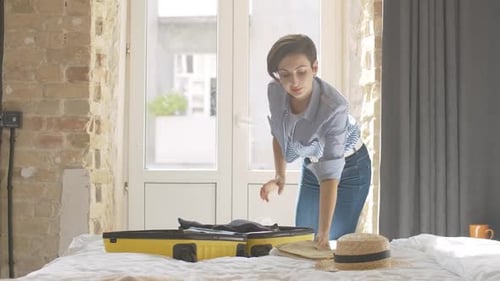 Woman Packing Yellow Suitcase in Bright Bedroom