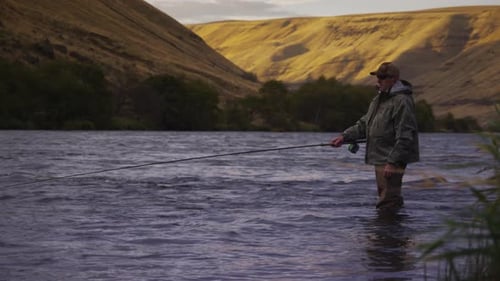 Man fly fishing in beautiful river at sunrise, rack focus