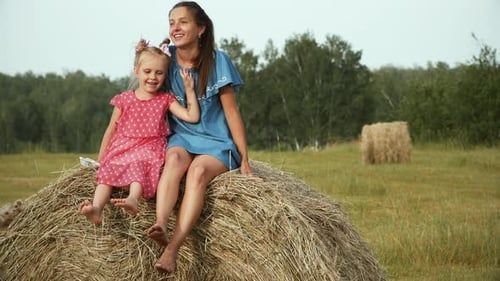 Mother and Daughter Sitting on Hay Bale in Field