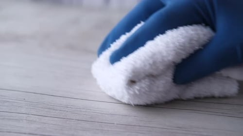 Gloved Hand Wiping a Table with a Cloth