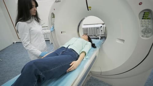 Female patient is undergoing CT or MRI scan under supervision of a radiologist