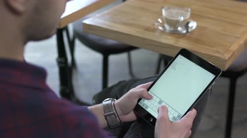 Young Adult Typing on Digital Tablet at Cafe