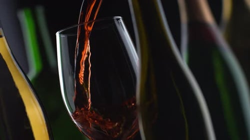 Red Wine Pouring into Glass with Bottles