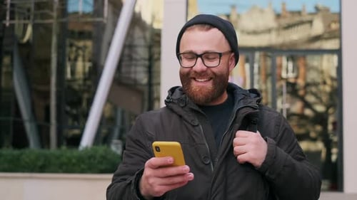 Crop View of Bearded Man in Glasses Looking at Phone Screen and Laughing While Walking at Street