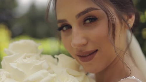 Beautiful Stylish Bride in White Wedding Dress and Veil Holding Wedding Bouquet in Hands in Park