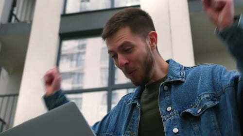 Surprised Man Getting Good News on Laptop Outside Business Center