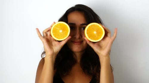 Woman Holds Orange Halves Playfully to Her Eyes