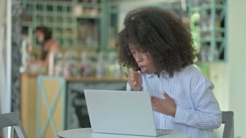 Sick African Businesswoman with Laptop Coughing in Cafe
