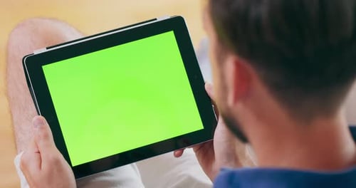 A Man Takes a Video Call on a Tablet Computer Which Features a Green Screen
