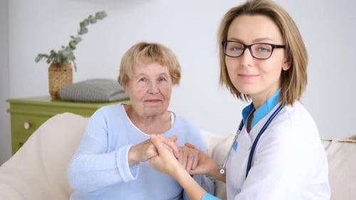 Doctor Comforting Senior Woman, Holding Hands Indoors
