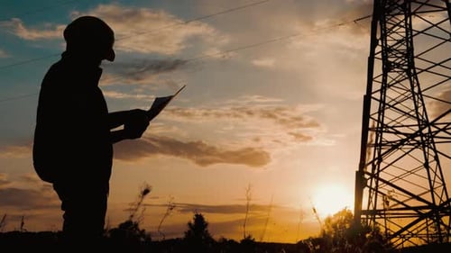 Silhouette of Engineer Standing on Field with Electricity Towers