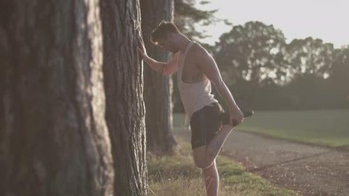 Man In Park Stretching Out His Legs Before He Goes For a Run Whilst Sun Sets Behind Him - Ungraded
