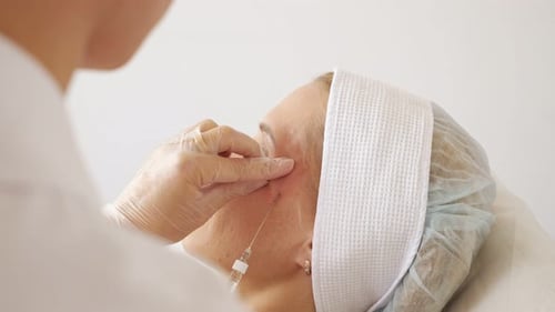 Side View of a Beautician Inserts a Needle Into a Woman's Temple