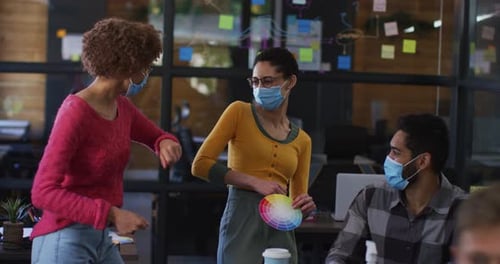 Diverse colleagues wearing face masks greeting each other by touching elbows at modern office