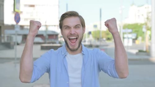 Young Man Celebrating with Arms Raised in City