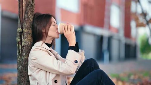 Relaxed Woman Drinking Coffee at Autumn City Park with Trees and Foliage