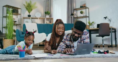 Padres que usan una computadora portátil mientras su hija dibuja