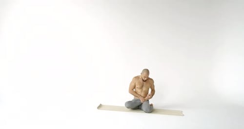 Ein erwachsener Glatzkopf sitzt in einer Lotusposition auf einer Yogamatte und übt Meditation in statischer Spannung