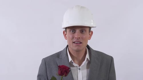 Retrato de homem genuíno tímido no capacete estende uma mão para a frente segurando a rosa vermelha