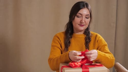 Woman Tying Red Ribbon on Wrapped Gift
