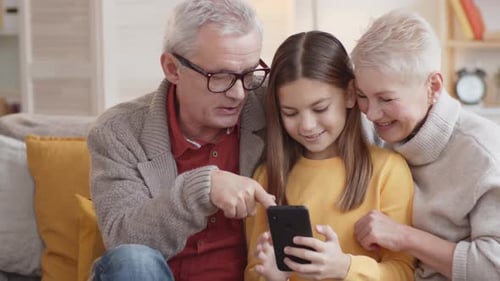 Girl Sharing Mobile Phone with Grandparents Indoors