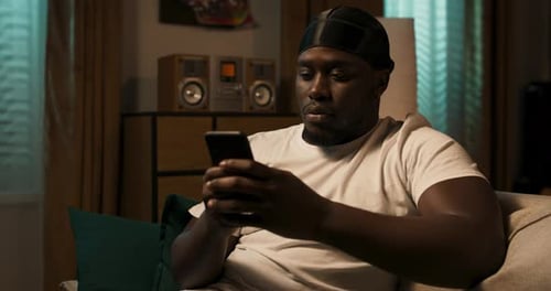 A Man Sits on the Sofa with a Smartphone in Hand in Spare Time Browsing Store Websites Installing