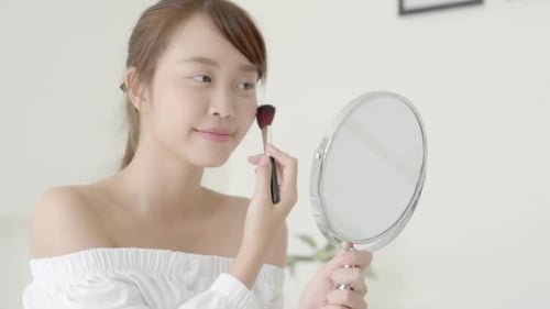 Woman Applying Makeup With a Brush in Mirror