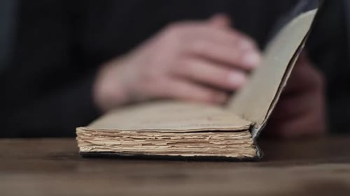 Closeup Front View of Unrecognizable Senior Aged Male Open Old Book and Turning Pages Sitting at
